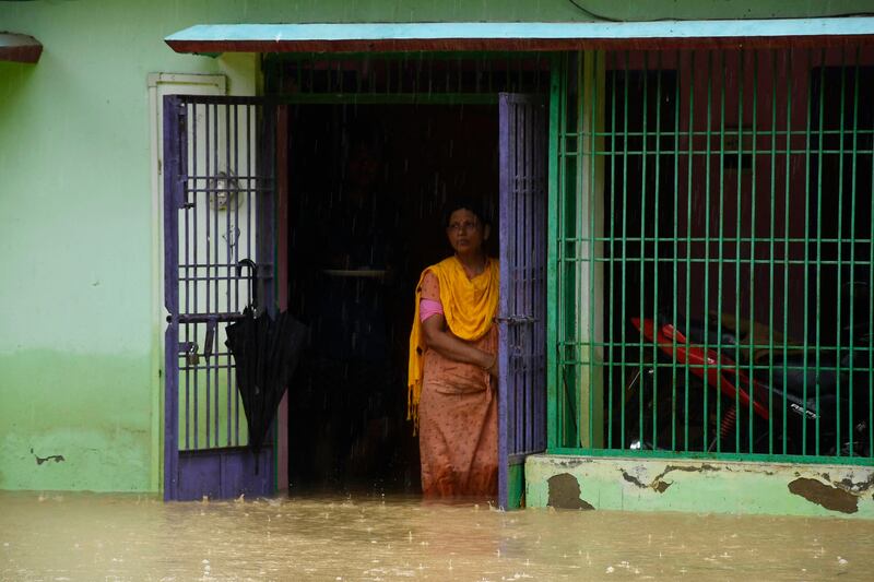 A woman looks out from the entrance of her flooded home in Kampur, Assam. AFP