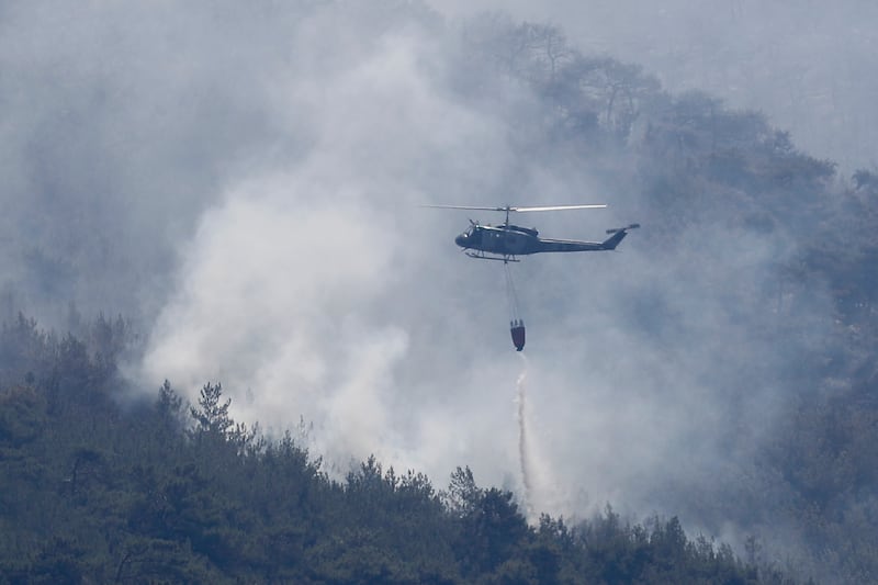 A Lebanese army helicopter drops water over a forest fire, at Qobayat village, in the northern Akkar province, Lebanon, Thursday, July 29, 2021.  Lebanese firefighters are struggling for the second day to contain wildfires in the country's north that have spread across the border into Syria, civil defense officials in both countries said Thursday.  (AP Photo / Hussein Malla)