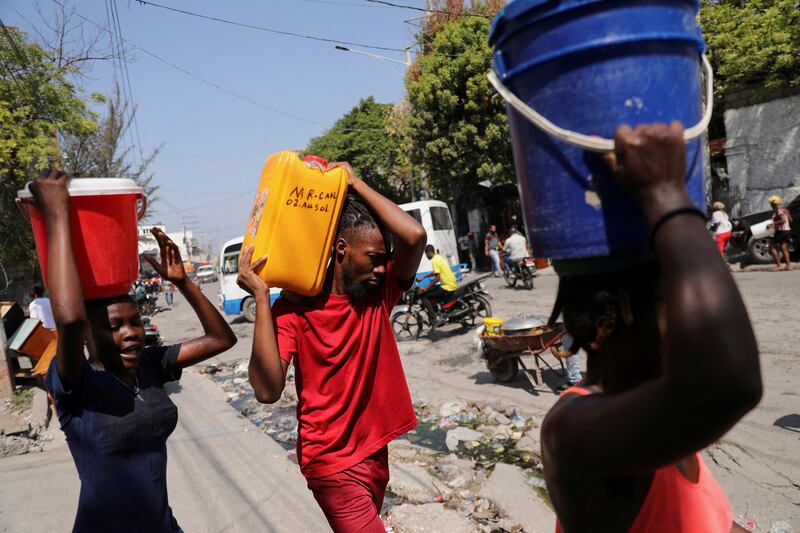 People carry water collected in containers in Port-au-Prince, Haiti, where gang violence has cut off food and fuel supplies. Reuters