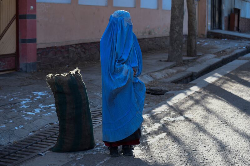 A burqa-clad woman stands next to a sack of charcoal donated by a volunteer team in Kabul. AFP.