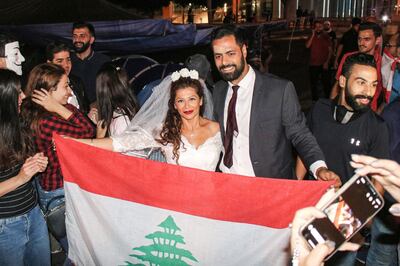 Malak Alaywe Herz, a woman who famously kicked the bodyguard of Education Minister Akram Chehayeb and became an icon in the current anti-government protests, poses for a picture in her wedding dress with a national flag alongside her newly-wed husband Mohammad after their marriage at Riad al-Solh square in the centre of the capital Beirut on October 23, 2019.  / AFP / Mohammad YASIN
