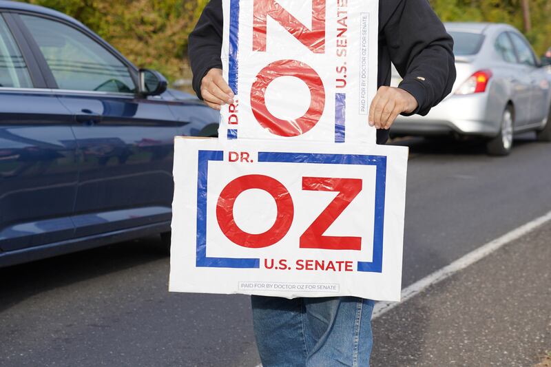 A protester uses two campaign signs to write out 'NO OZ'.