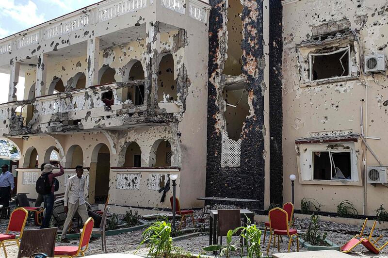A man passes in front of the rubbles of the popular Medina hotel of Kismayo on July 13, 2019, a day after at least 26 people, including several foreigners, were killed and 56 injured in a suicide bomb and gun attack claimed by Al-Shabaab militants. A suicide bomber rammed a vehicle loaded with explosives into the Medina hotel in the port town of Kismayo before several heavily armed gunmen forced their way inside, shooting as they went, authorities said. / AFP / STRINGER

