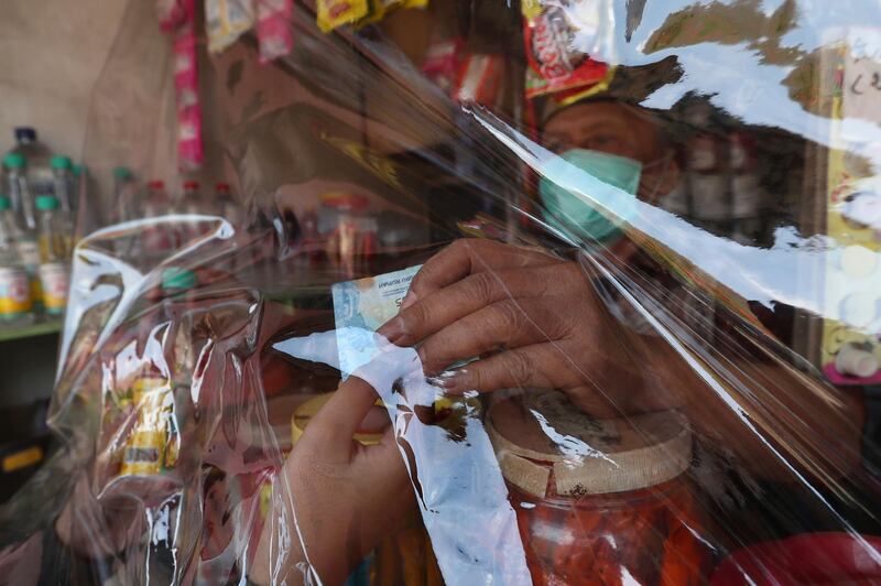 A shop owner receives money from a customer behind a sheet of protective plastic at a convenience store in South Tangerang on the outskirts of Jakarta, Indonesia. AP Photo