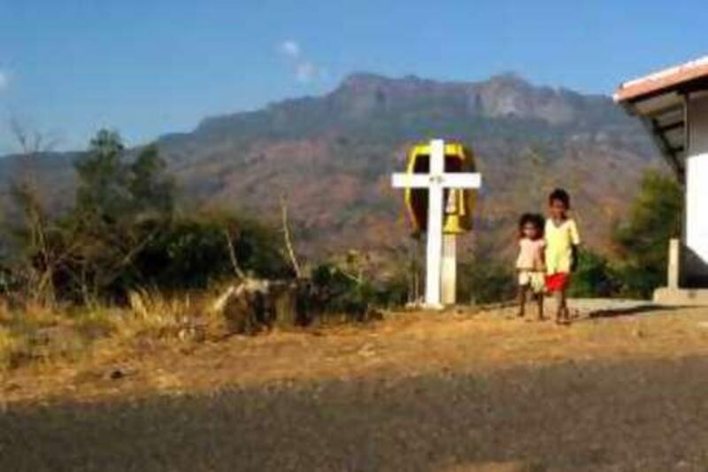 Two children pass one of the Stations of the Cross in Maliana. Far from the capitol of East Timor, this isolated town is ruled largely by the Catholic Church in all spiritual matters. Lately evangelical religions have been trying to find a home in Maliana, but the powerful Church has shut them down and driven the pastors from their homes. Jesse Wright/The National *** Local Caption ***  children and a cross.jpg