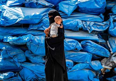 TOPSHOT - A woman wearing a niqab (full face veil) walks carrying an infant at al-Hol camp for displaced people in al-Hasakeh governorate in northeastern Syria on July 22, 2019, as people collect UN-provided humanitarian aid packages.  / AFP / Delil souleiman
