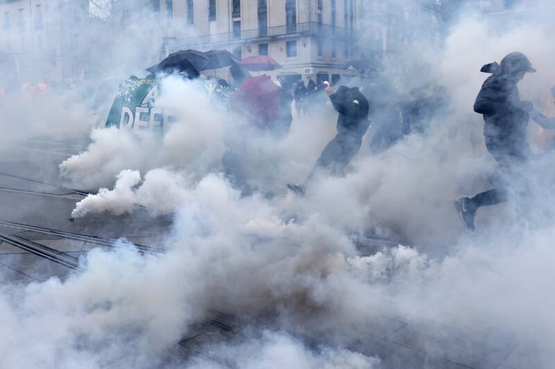 Youths run though clouds of tear gas at a protest in Nantes, western France. AP