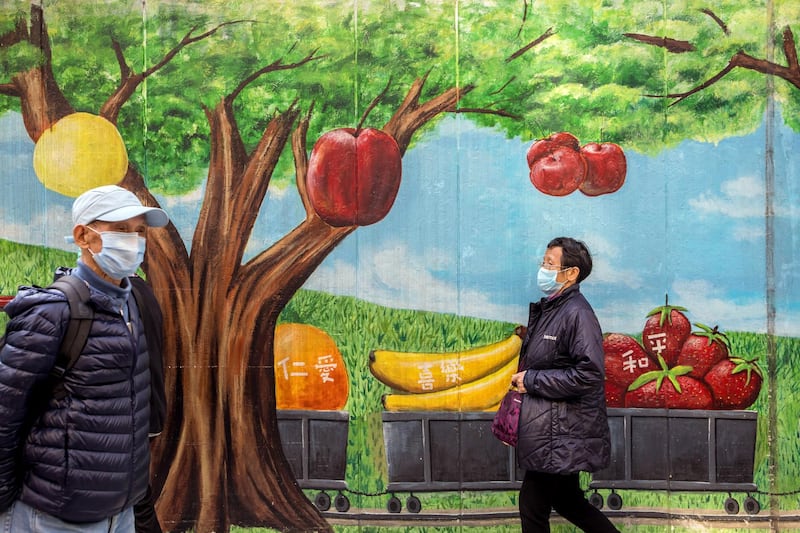 Pedestrians wearing protective masks walk past a mural featuring fruits in Hong Kong, China. Bloomberg