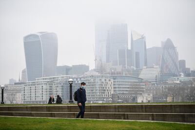 A man walks along the embankment of the River Thames in south London on March 2, 2021, with the skyline of the City of London in the background. / AFP / JUSTIN TALLIS
