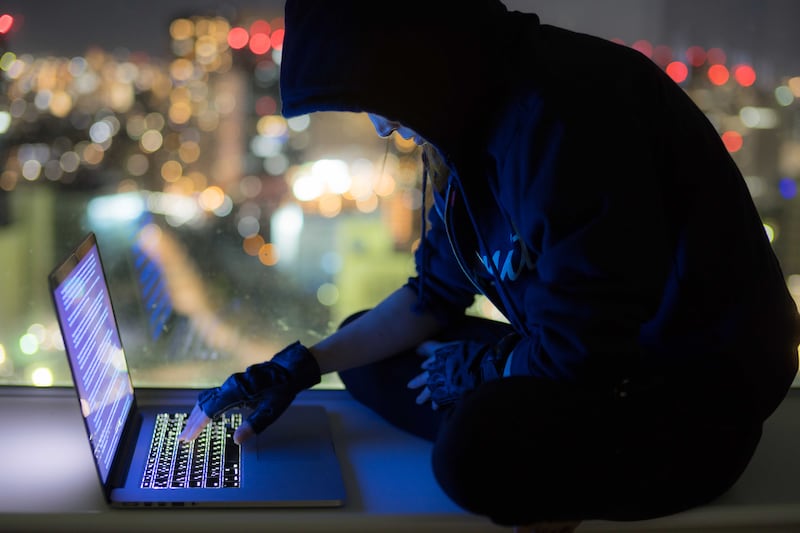 Woman in hooded sweater operating PC in dark with city in background. Getty Images