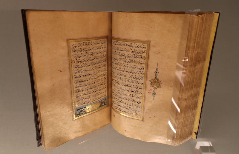 A manuscript of the Quran, in black Naskh script, accentuated with red detailing, chapter headings and margins highlighted in gold.