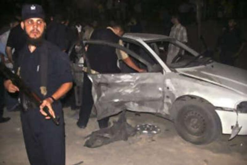 A Palestinian Hamas police officer stands guard as others inspect a damaged car following the explosion in Gaza City.