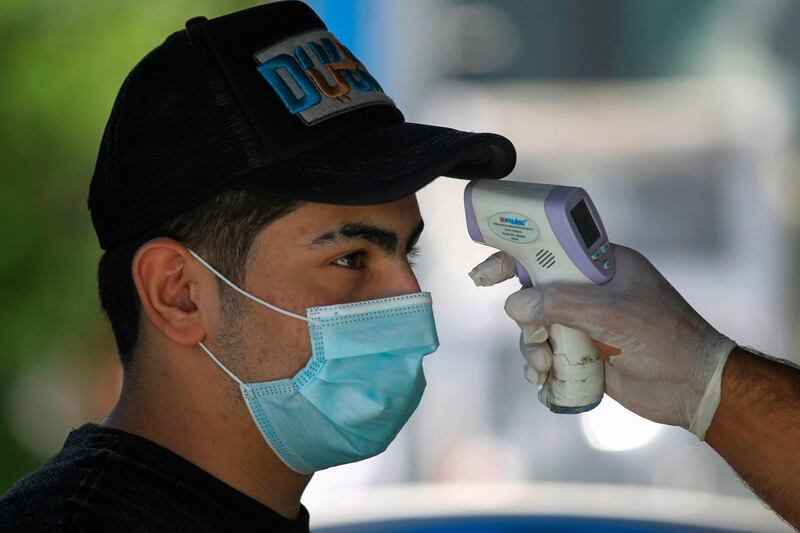 A customer, wearing a protective mask, gets his temperature checked before entering a supermarket in the Iraqi capital Baghdad.   AFP