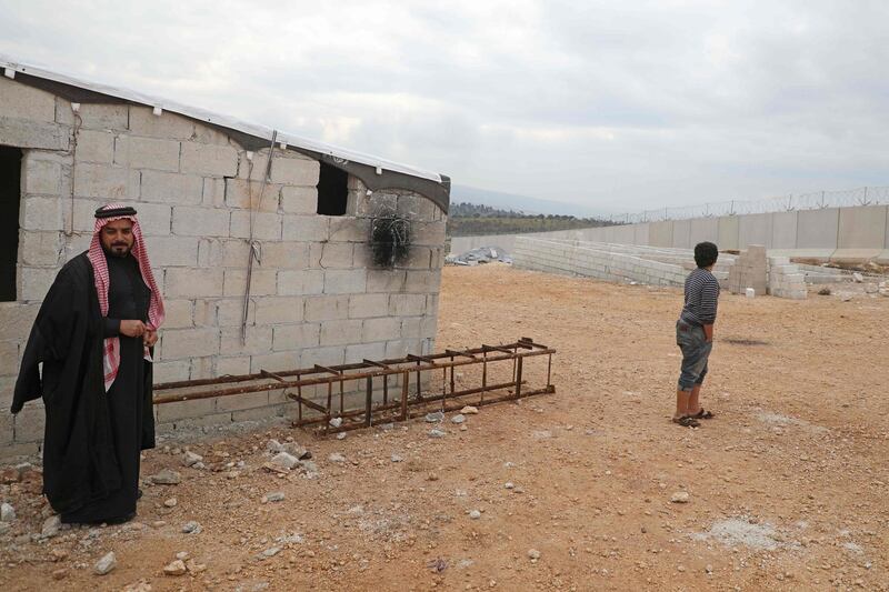 Syrian Abu Jaber stands next to a ladder which he created to climb over the Turkish border wall (L), at an informal camp in Kafr Lusin village in Syria's northwestern province of Idlib, on February 21, 2020. Six months ago, the family fled deadly fighting in Idlib province of northwest Syria, seeking shelter near the border village of Kafr Lusin, where dozens of families live in an informal camp for the displaced. Turkey, which already hosts the world's largest number of Syrian refugees with around 3.6 million people, has placed barbed wire and watchtowers along the wall to prevent any more crossings.
 / AFP / AAREF WATAD
