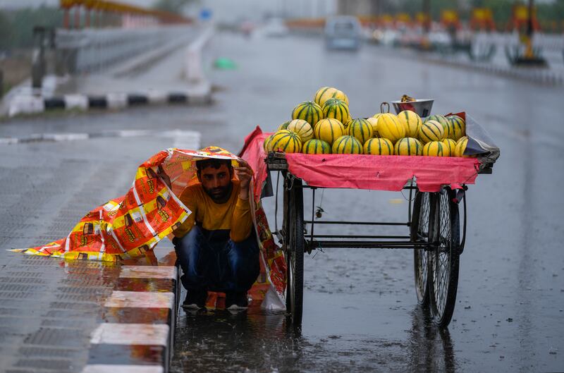 An Indian fruit seller shelters from the rain under a plastic sheet in Jammu. AP