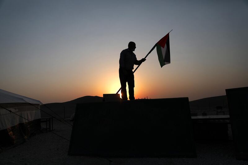 A man raises a Palestinian flag at tent school area on the third day of the school year, at Am Kusa Bedouin community, south of the West Bank city of Hebron.  EPA