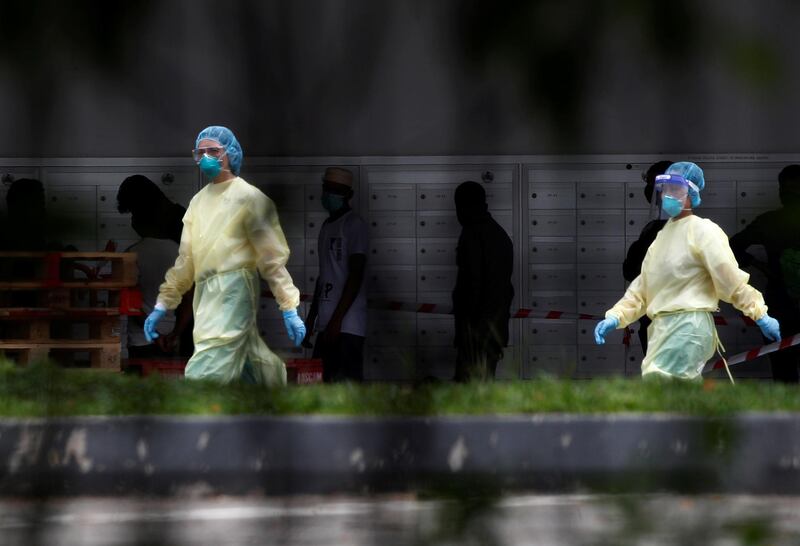 Medical personnel walk past migrant workers at a dormitory during the coronavirus (COVID-19) outbreak in Singapore. REUTERS