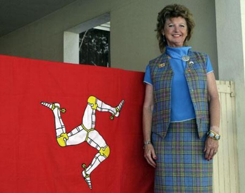 Gil Costain-Salway stands beside the Isle of Man flag at her residence in Dubai. The former airline worker runs quizzes every month for the Dubai Manx Society.
