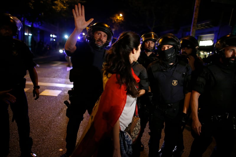 A woman wearing a Spanish flag over her shoulders walks in front of a line of Catalan riot police as anti-independence supporters march against the unilateral declaration of independence approved earlier by the Catalan parliament in downtown Barcelona Friday, Oct. 27, 2017. Catalan lawmakers voted Friday to secede from Spain, shortly before Spain's Senate approved a request by the central government to take direct control of Catalonia's affairs. (AP Photo/Manu Fernandez)