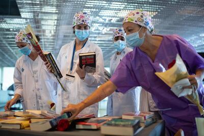 Healthcare workers holding roses pick up books donated to the field hospital of Hotel Catalonia Fira in Barcelona on April 23, 2020 during the Sant Jordi festivities marking Saint George's day. Traditionally men give women roses and women give men a book to celebrate the Catalan holiday also know as "The Day of the Rose" or "The Day of the Book". Spain said 440 people died in the past 24 hours from the new coronavirus, a slight increase for the third day running, bringing the overall death toll to 22,157. / AFP / Josep LAGO
