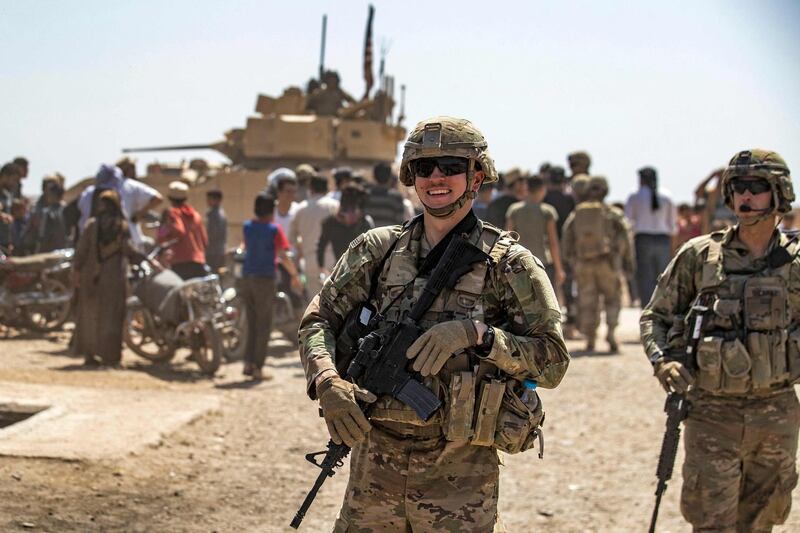 US soldiers on patrol in Rmelan, as in the background locals gather round a Bradley Fighting Vehicle. AFP