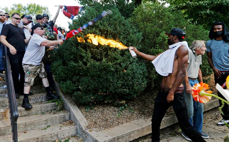 FILE - In this Aug. 12, 2017 file photo, a counter demonstrator uses a lighted spray can against a white nationalist demonstrator at the entrance to Lee Park in Charlottesville, Va. The deadly white nationalist demonstration in Virginia has brought new attention to an anti-fascist movement whose black-clad, bandana-wearing members have been a regular presence at protests around the country in the last year. Members of the antifa movement were among those protesting the Charlottesville rally last weekend. (AP Photo/Steve Helber, File)