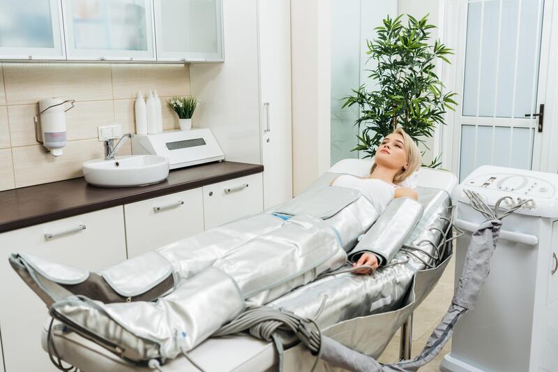 T322C8 Blonde girl lying on beauty couch during pressotherapy session in clinic. Alamy