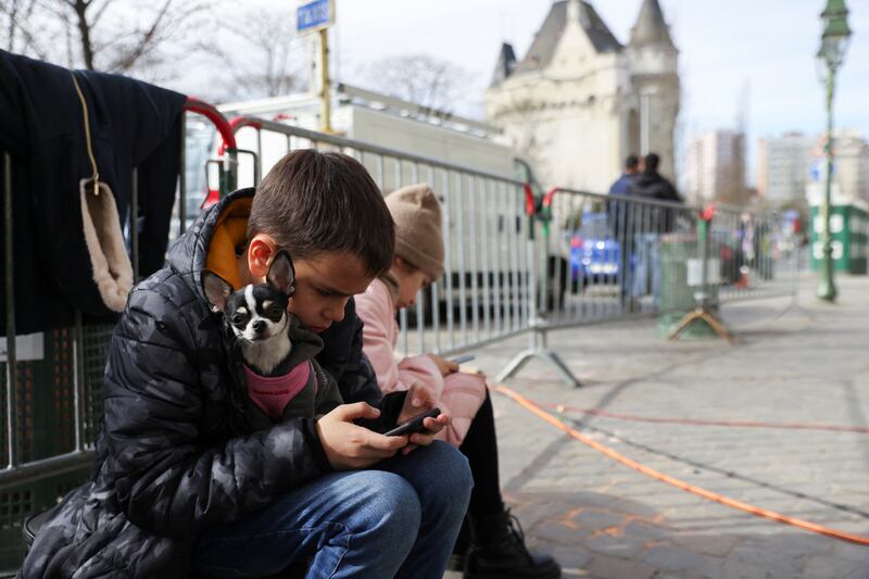 Children look at phones as people who fled the conflict in Ukraine wait outside an immigration office in Brussels, Belgium. Reuters