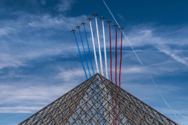 French elite acrobatic flying team "Patrouille de France" (PAF) release smoke in the colours of the French flag as they perform a fly-over the Louvre Pyramid during the Bastille Day military parade in Paris on July 14, 2022.  (Photo by Martin BUREAU  /  AFP)