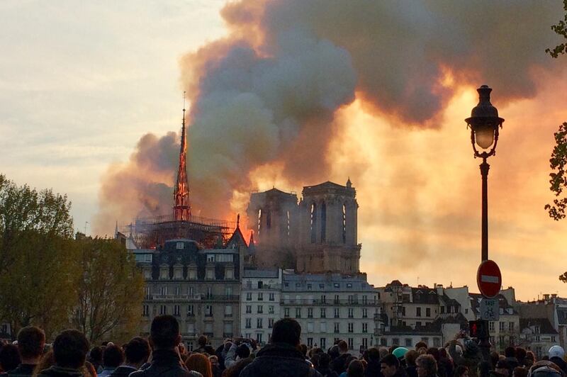 A picture taken with a mobile phone shows people looking at smoke and flames rising during a fire at the landmark Notre-Dame Cathedral in central Paris on April 15, 2019, potentially involving renovation works being carried out at the site, the fire service said.

 / AFP / Edouard MAGRINO
