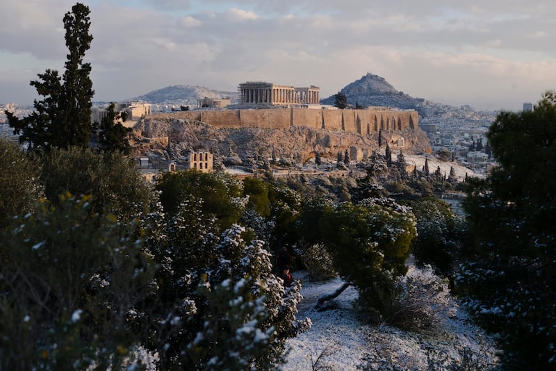 A man walks at Filopappos hill as at the background is seen the ancient Acropolis hill with the 500BC Parthenon temple, after a snowfall in Athens , on Tuesday, Jan. 8, 2019. (AP Photo/Petros Giannakouris)