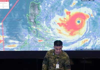 A member of the Philippine Air Force stands in front of a satellite image of Typhoon Mangkhut, locally named Typhoon Ompong, at the National Disaster Risk Reduction and Management Council operations center in metropolitan Manila, Philippines on Thursday, Sept. 13, 2018. Philippine officials have begun evacuating thousands of people in the path of the most powerful typhoon this year, closing schools and readying bulldozers for landslides. (AP Photo/Aaron Favila)