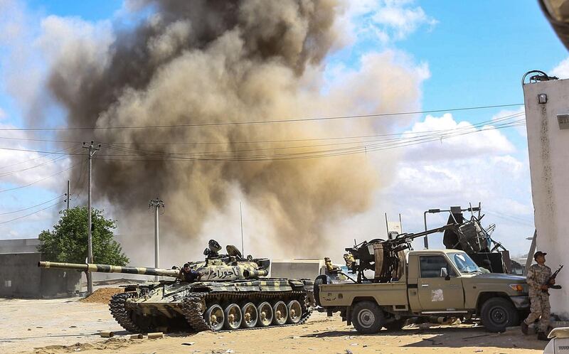 This picture taken on April 12, 2019 shows a smoke plume rising from an air strike behind a tank and technicals (pickup trucks mounted with turrets) belonging to forces loyal to Libya's Government of National Accord (GNA), during clashes in the suburb of Wadi Rabie about 30 kilometres south of the capital Tripoli.  / AFP / Mahmud TURKIA
