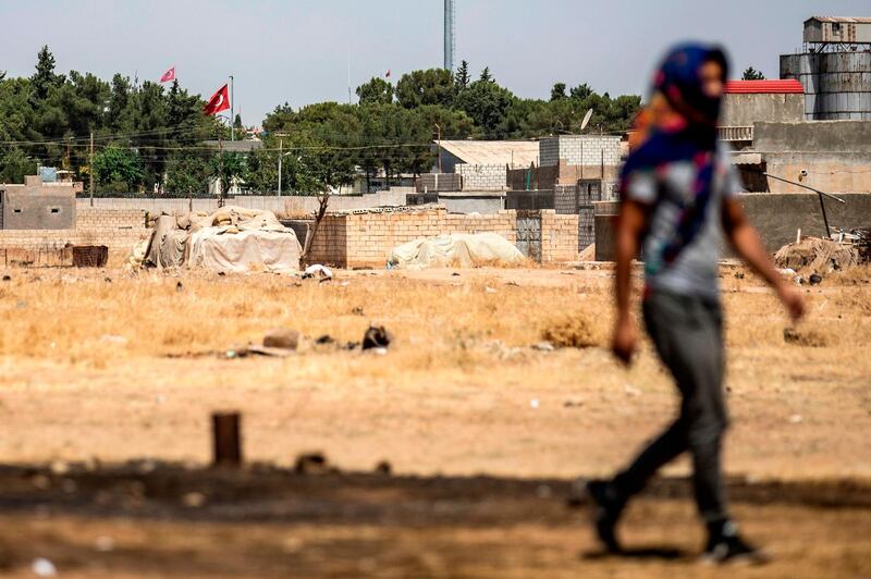 A Syrian Kurd walks during a protest and sit-in against Turkey, in the town of Ras al-Ain in Syria's Hasakeh province near the Turkish border on August 9, 2019, with the flags of Turkey seen across the border in the background.  / AFP / Delil SOULEIMAN
