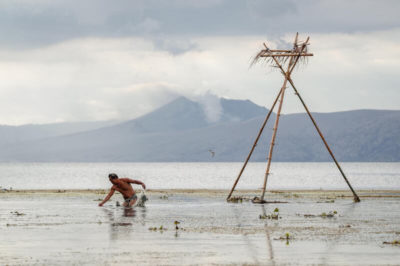 A man fishes as the Taal volcano spews smoke in Balete, Batangas on January 17. EPA