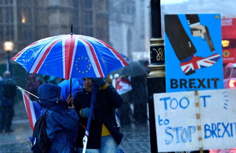Brexit protesters shelter under an umbrella outside the Houses of Parliament. EPA