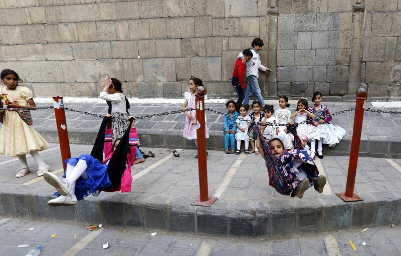 Yemeni children play a cloth hammock swing hung with a chain barrier set up around a mosque in the old quarter of Sana'a, Yemen.  EPA