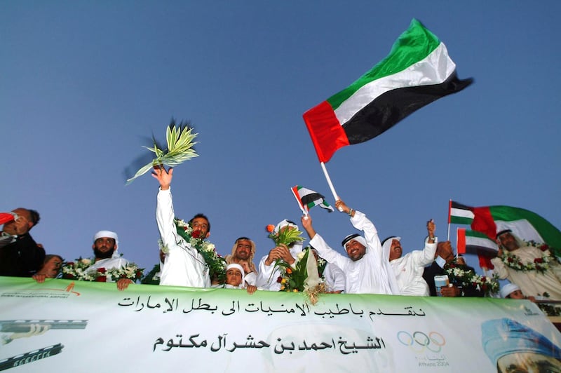 Sheikh Ahmed bin Hashr Al-Maktoum (3rd L), 40, a member of Dubai's ruling family, salutes 26 August 2004 a crowd of cheerful Emirati citizens who received him upon arriving in Dubai after winning a historic first gold medal during the Athens Olympics in the men's double trap shooting. Al-Maktoum became the first athlete from the UAE to win an Olympic medal of any colour with a superb display of shooting at the Markopoulo Shooting Centre in Athens. AFP PHOTO/Nasser YOUNES (Photo by NASSER YOUNES / AFP)