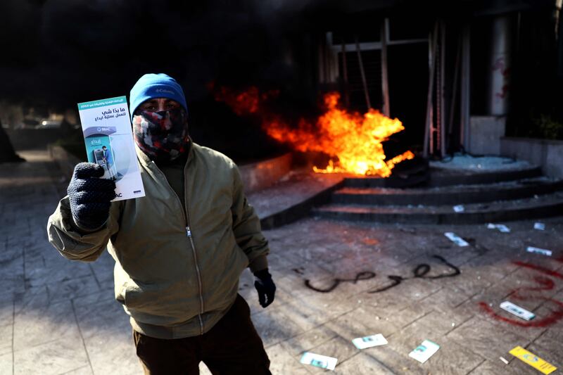 A protestor stands in front of burning tyres and Arabic graffiti on the ground that reads 'thieves' outside a bank in Beirut. AFP