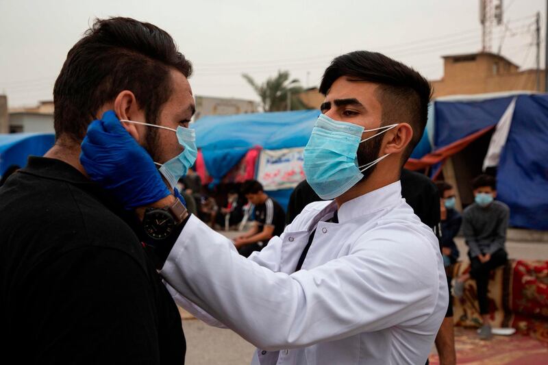 An Iraqi student shows an anti-government demonstrator how to wear a protective mask during a rally in the southern Iraqi city of Basra.  AFP