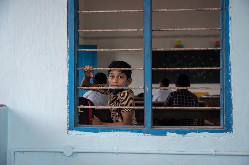 A schoolboy waiting for classes to begin looks through a classroom window.
