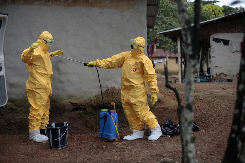 Mr Kamara, left, is sprayed by his co-worker, Konah Deno, after they load six patients suspected to have been infected by the Ebola virus into their ambulance in the village of Freeman Reserve. Both men are donning their yellow protective suits and eye goggles.