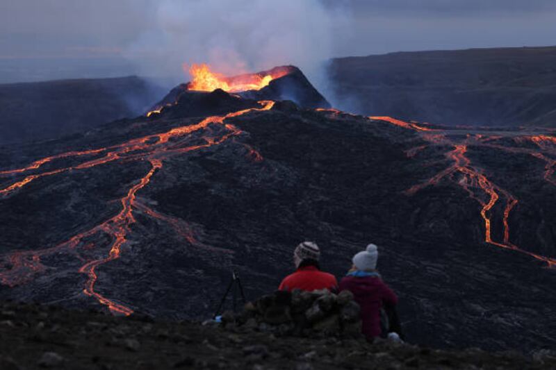 A couple sitting on a hill watch as the Fargradalsfjall volcano spews molten lava.  Getty Images