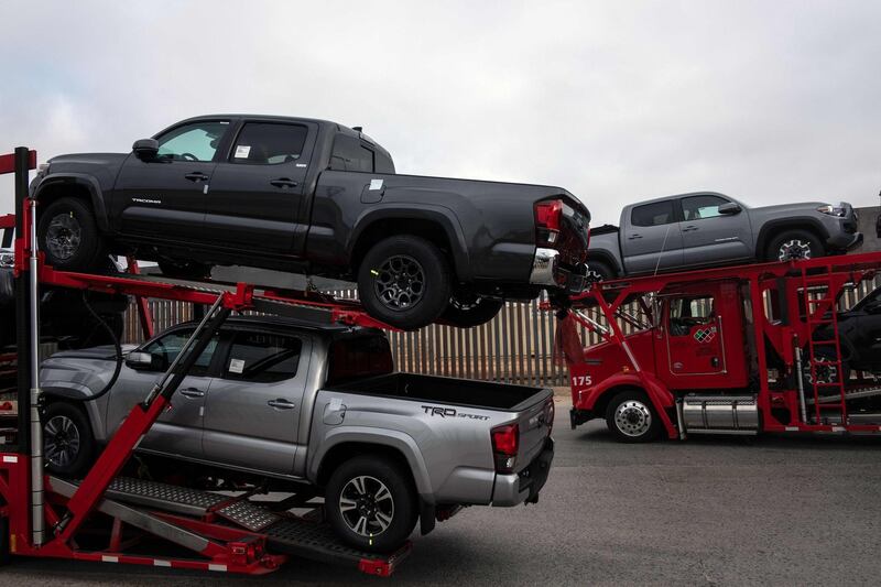 Trucks loaded with new trucks drive next to the US/Mexico border fence at the Otay commercial Port of entry in Tijuana, Baja California state, Mexico on August 27, 2018. - Mexican President-elect Andres Manuel Lopez Obrador's advisers on Monday hailed a new trade deal with the United States, saying it represented progress on energy and wages for Mexico's workers. (Photo by Guillermo Arias / AFP)