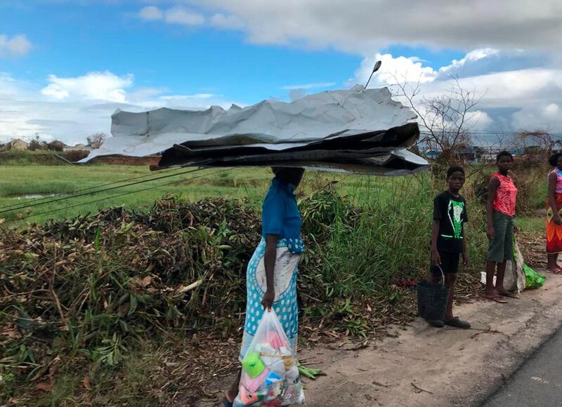 A woman carries salvaged metal sheeting amid the shattered city of Beira. AP Photo