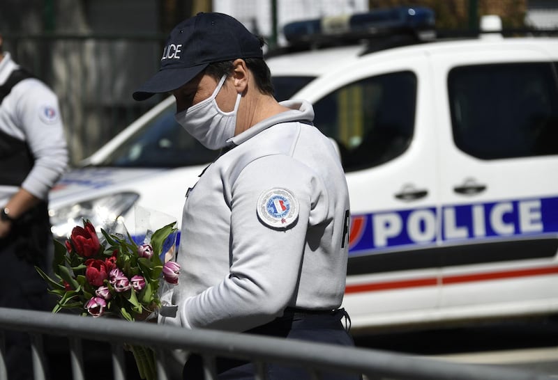 A Police officer holds flowers brought by people, to be taken down to the police station where a police official was stabbed death Friday, in Rambouillet, south-west of Paris, on April 25, 2021. French prosectors opened a terror probe after a woman working for the police was stabbed to death in Rambouillet, a well-heeled usually peaceful commuter town about 60 kilometres (40 miles) from Paris. The attack revived the trauma of a spate of deadly attacks last year in France blamed on Islamist radicals. / AFP / Bertrand GUAY
