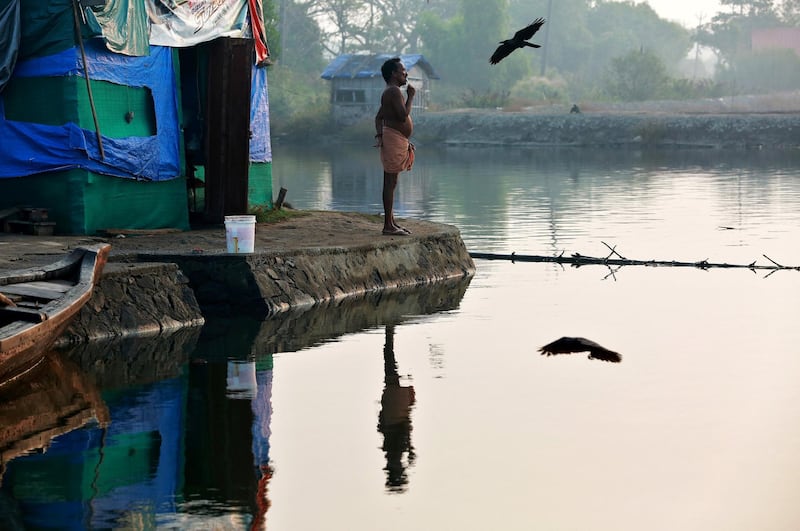 A fisherman brushes his teeth as he stands outside a temporary shelter on the bank of Periyar River, on the outskirts of Kochi, India.  Sivaram V / Reuters