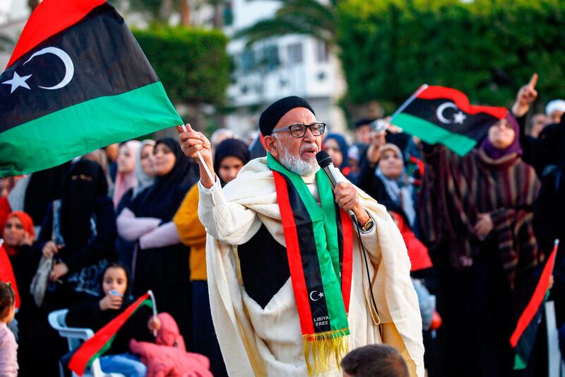 A man holding up a Libyan national flag and wearing a matching scarf speaks in a microphone during a demonstration against eastern strongman Khalifa Haftar, and in support of the UN-recognised government of national accord (GNA), in the Martyrs' Square in the GNA-held capital Tripoli on December 27, 2019.  / AFP / Mahmud TURKIA
