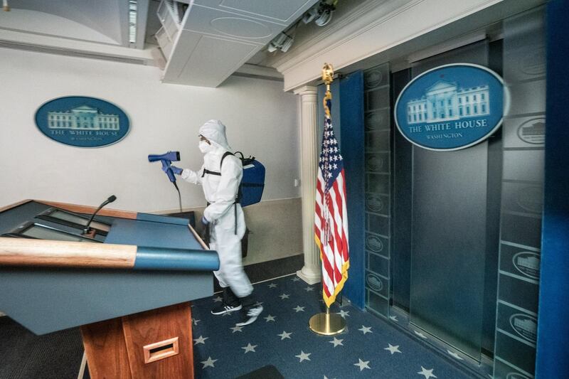 A cleaner at the White House sprays disinfectant in the James Brady Press Briefing room after US President Donald Trump return to the White House.  EPA