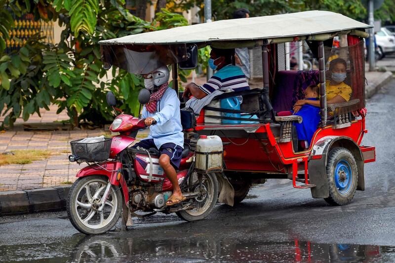 Tuk-tuk driver and passengers wear protective facemasks while travelling on street in Phnom Penh, Cambodia.
 AFP